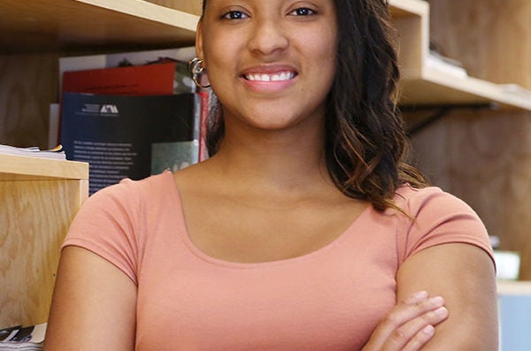 Student standing and smiling with arms crossed, appearing confident