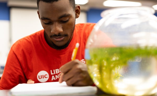 Student wearing red UIC t shirt writing in a notebook